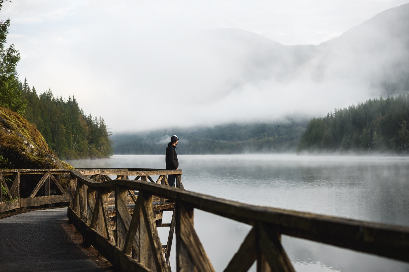 A person stares out at Inland Lake from a bridge lookout on a misty day