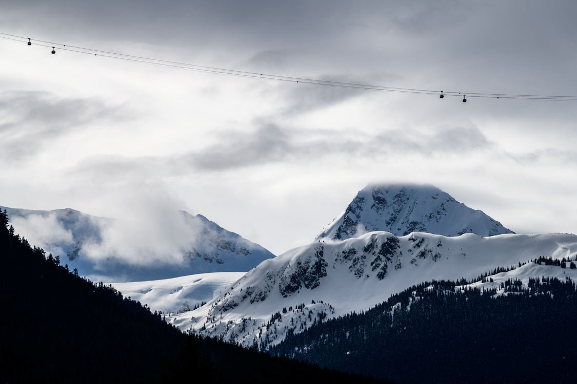 Whistler Blackcomb's world record breaking PEAK 2 PEAK Gondola strung out across the valley with a large, snow-capped peak in the background.