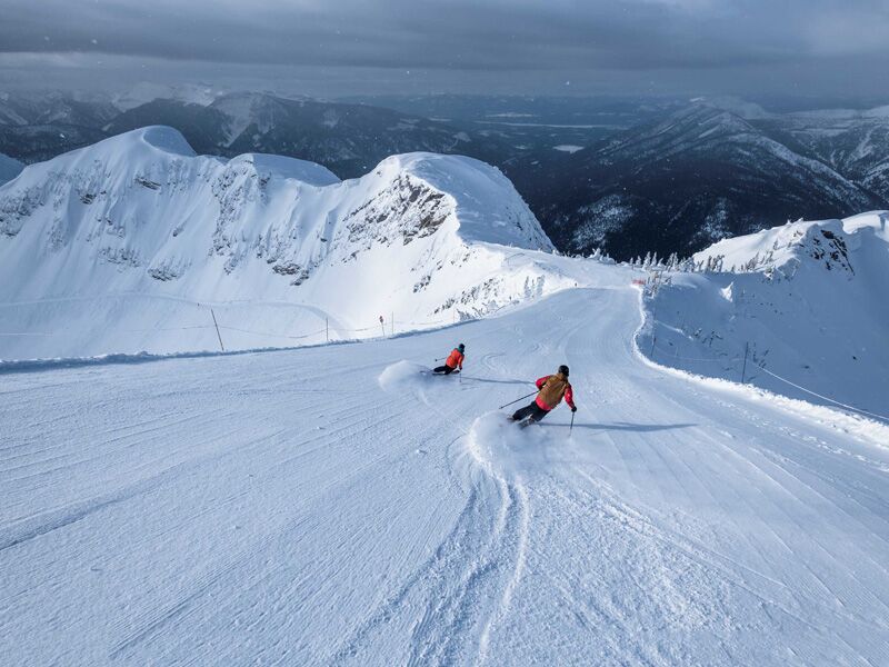 Two skiers head down a trail at Fernie Mountain on a groomed run.