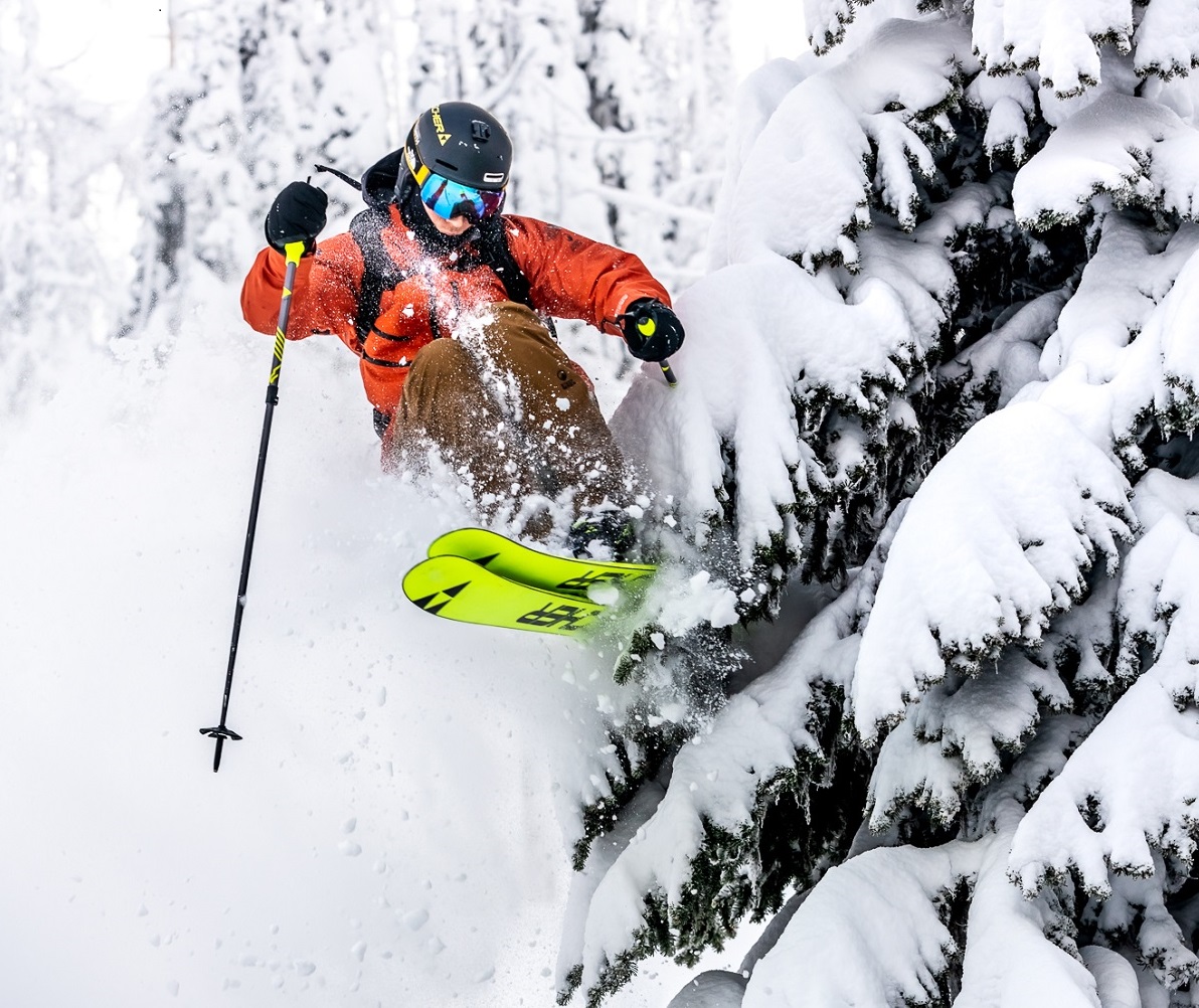 A skier makes a jump next to a tree in deep snow at Whitewater Ski Resort