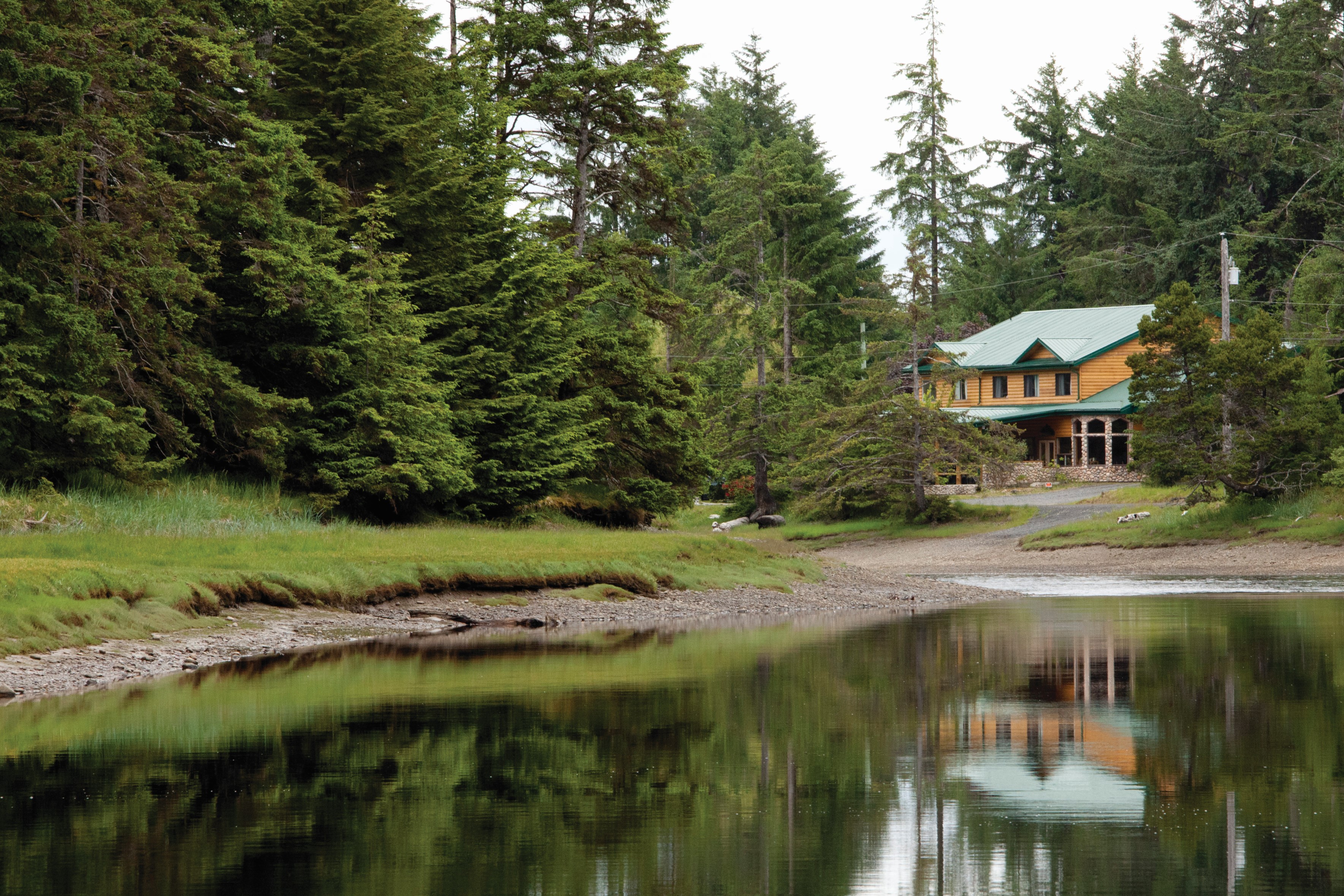 Outside of Haida House seen between the trees. The building reflects of the lakes edge.