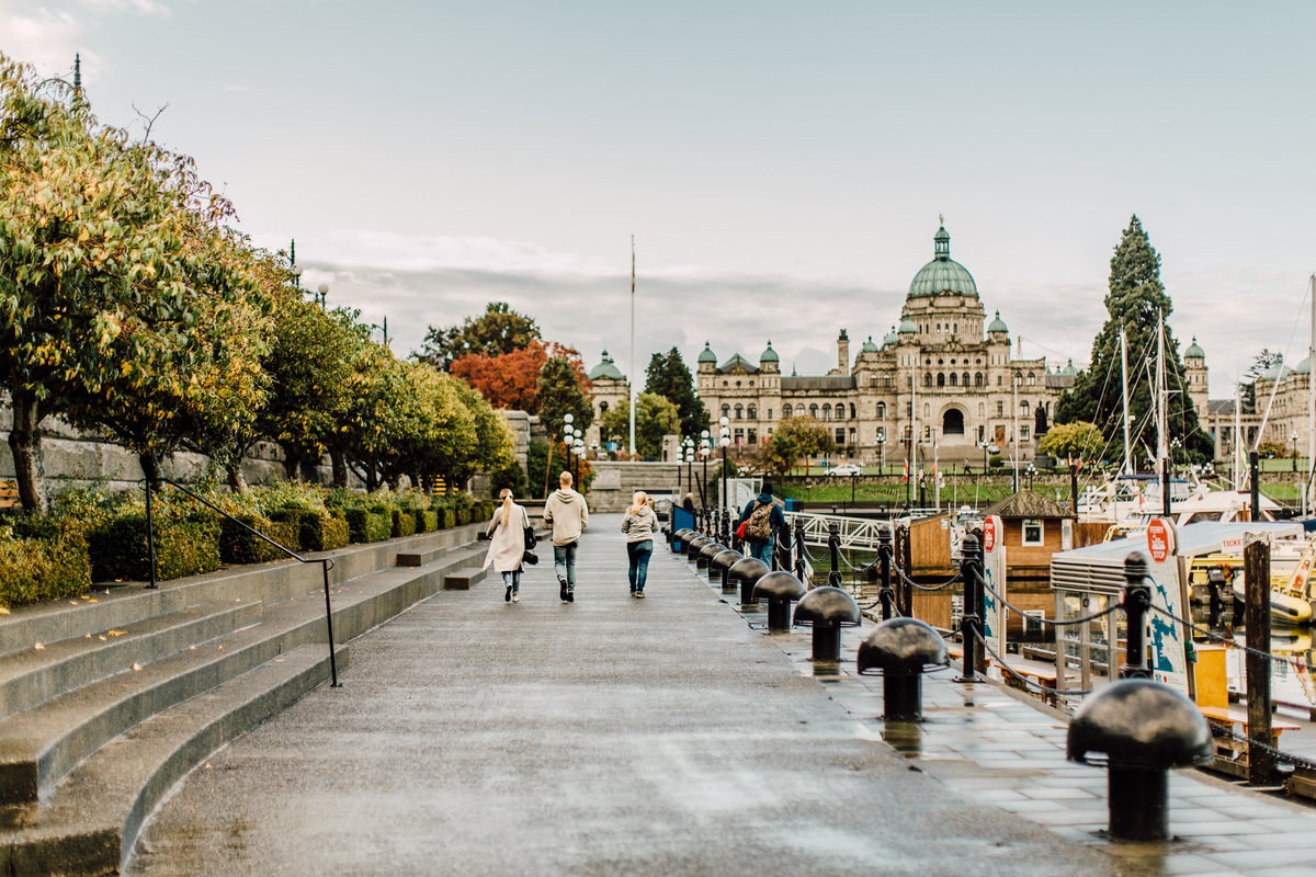 Four people walk down by the Victoria Inner Harbour front by the Parliament buildings