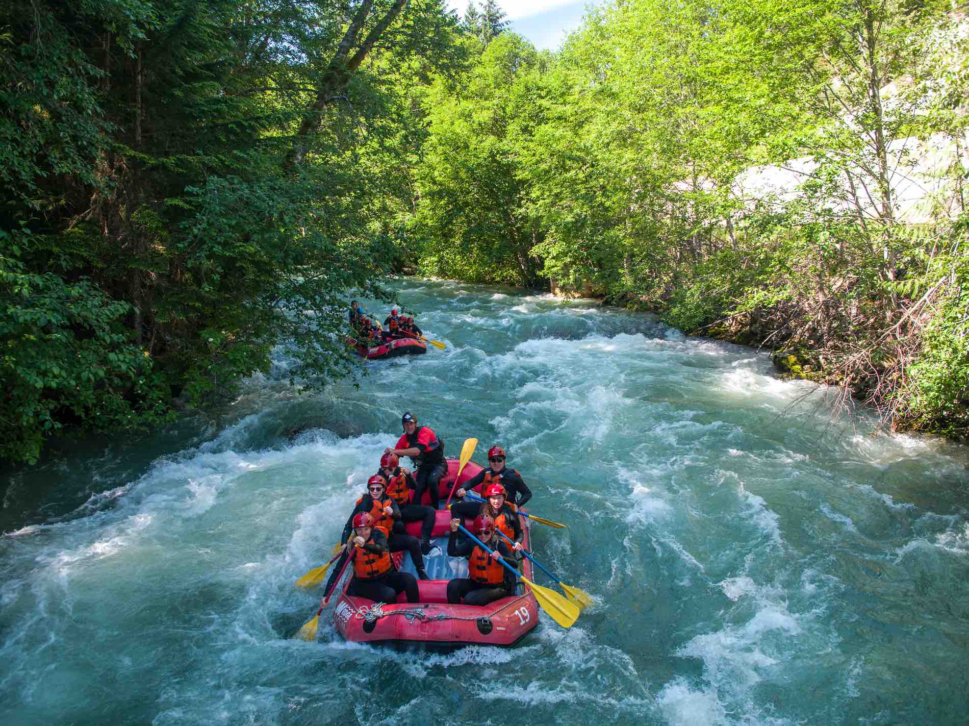 Two red rafts are paddled down a moving river in Whistler. Each raft has a guide and up to 8 eight rafting guests.