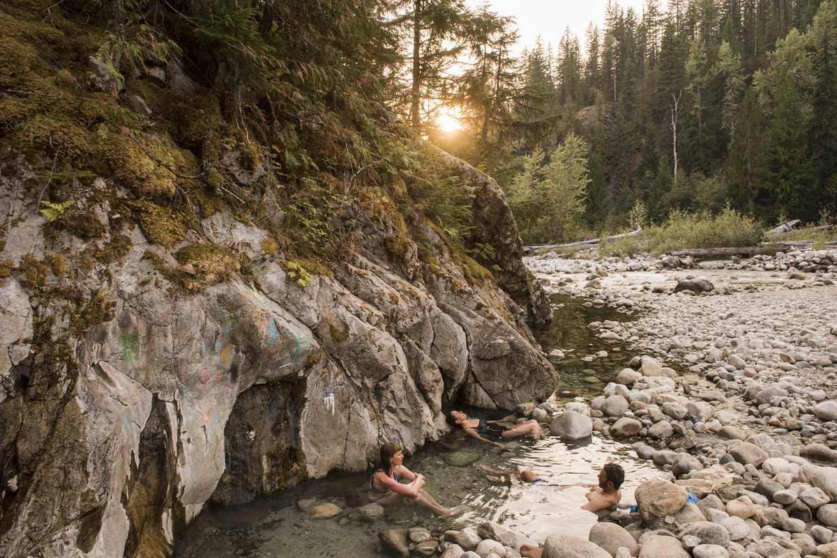 Tourists soak in the lower pools at the Halfway River Hot Springs. These natural hot springs are surrounded by rocky pools in the forest.